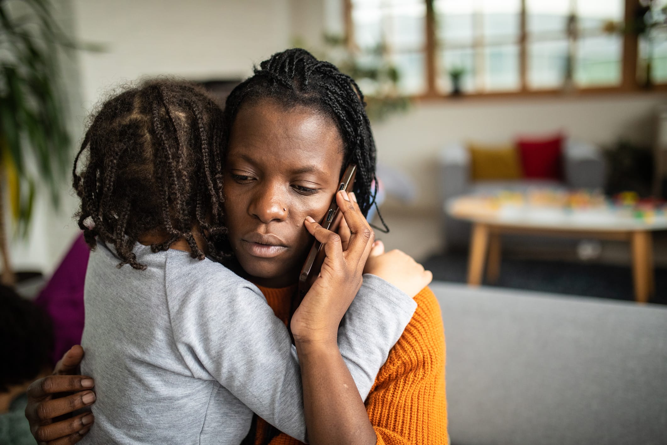 Black woman using phone while embracing her daughter at home