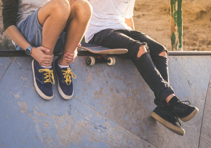 Close up of two young boys sitting on half pipe ramp, after nice tricks and jumps at the skatepark. Trendy teenagers enjoying free time at the skate park. Youth, togetherness and friendship concept.